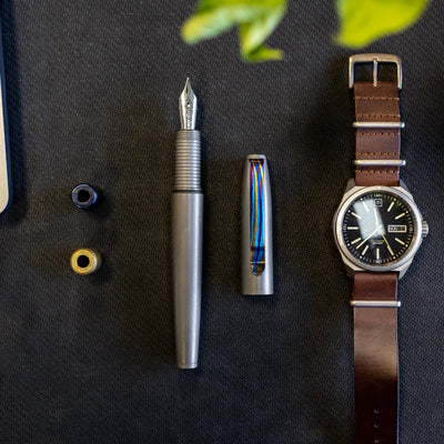 Big Idea Design LLC fountain pen with titanium Damascus pen clip and colorful cap on black surface