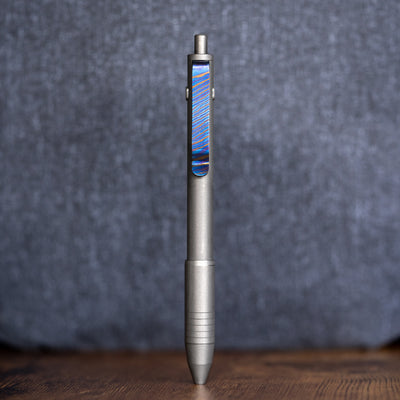 Big Idea Design LLC sleek titanium EDC pen with blue accented clip on wooden surface