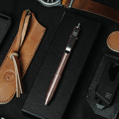 Big Idea Design LLC titanium EDC pen displayed on black box with leather accessories and watch