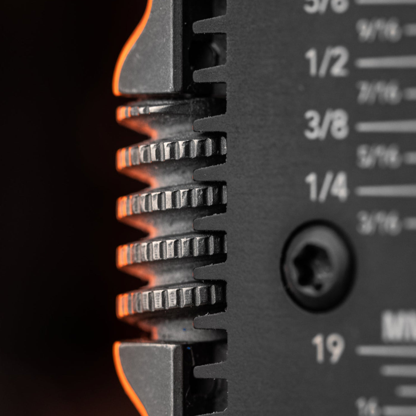 Close-up of titanium EDC wrench gear teeth and measurement markings on black metal surface