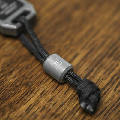 BIG IDEA DESIGN LLC titanium lanyard bead on black paracord against wooden background
