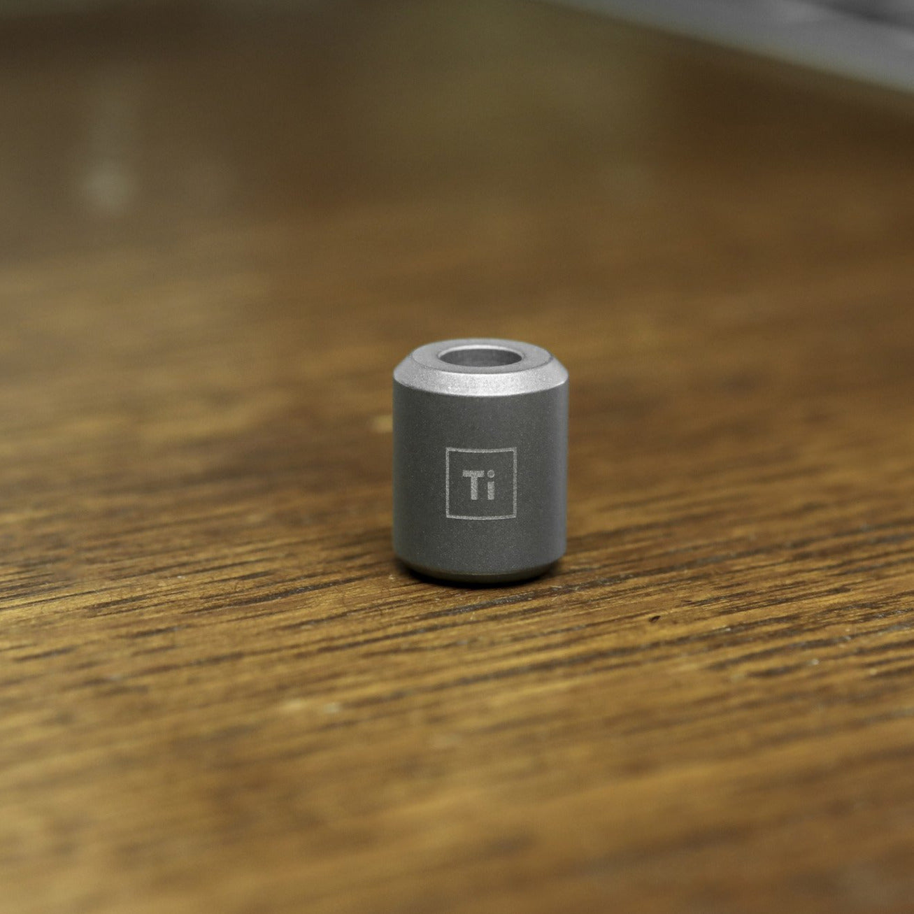BIG IDEA DESIGN LLC titanium lanyard bead in gray metal with chemical symbol Ti on wood surface