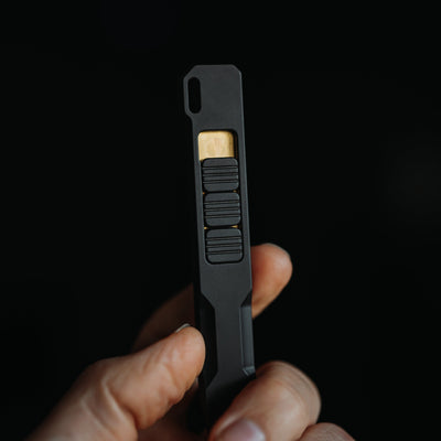 Black titanium pry bar tool held between fingers with textured grip and gold accent