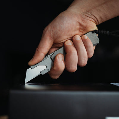 Hand holding a titanium utility knife cutting on a dark surface with black background