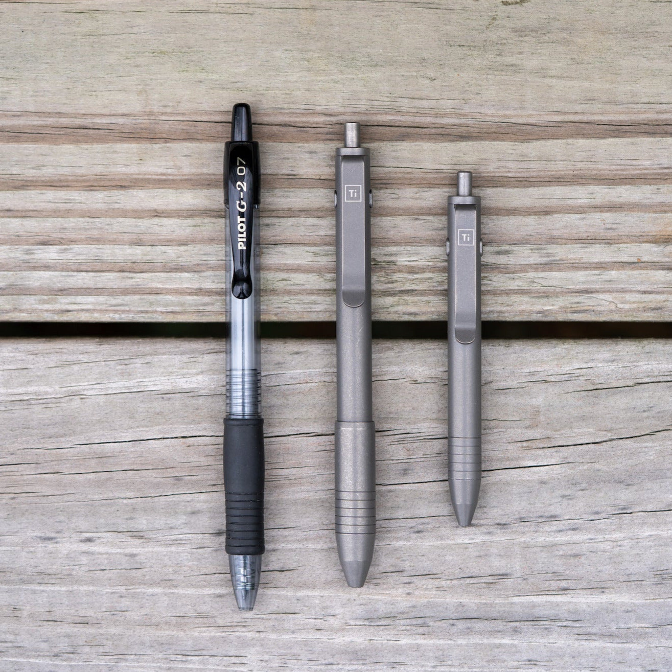 Big Idea Design LLC EDC pen titanium set alongside a black Pilot G-2 07 pen on wooden surface